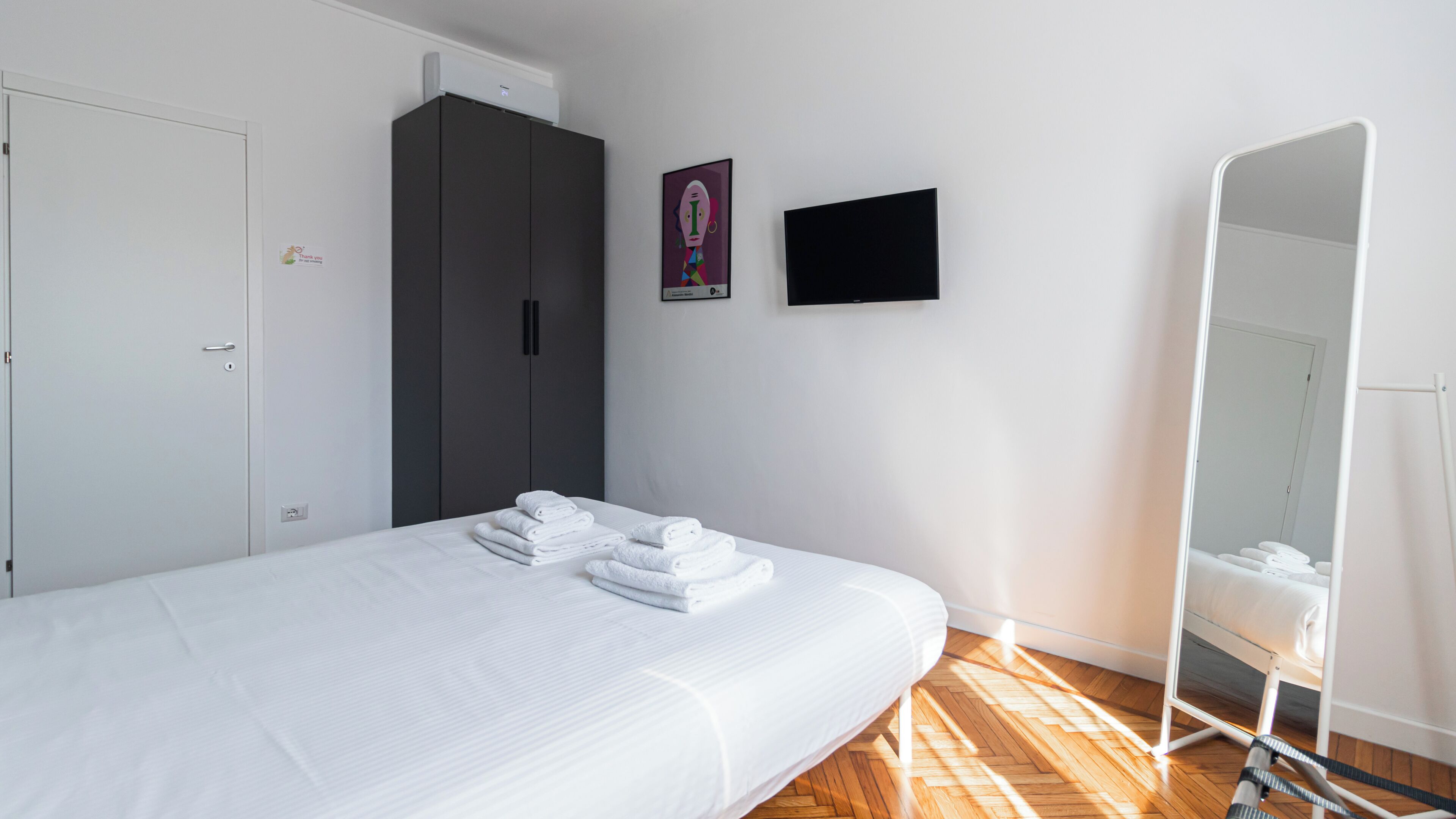 A bedroom with a bed, a wardrobe, a flat-screen TV, and a mirror.