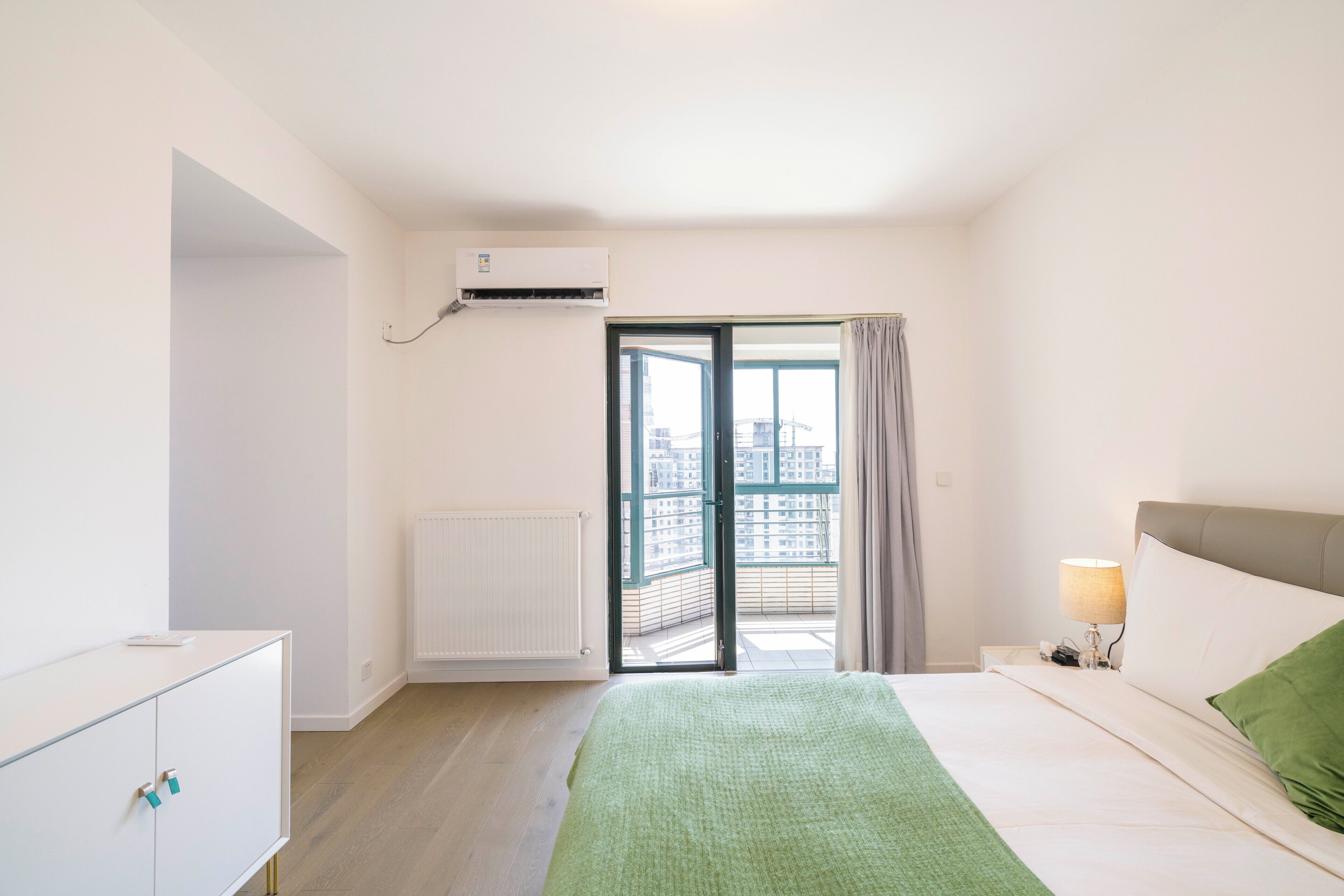 Un dormitorio con cama, mesita de noche con lámpara, armario y puerta corrediza de vidrio que da a un balcón.