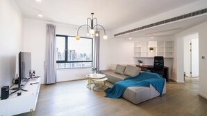 A modern living room with a sofa, a small round table, a TV, and a large window with a city view. - Tyms Elegant 4BR 2BA Apt in Xujiahui (Shanghai)