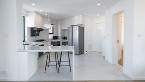 A modern kitchen with white cabinetry, a central island with stools, a stainless steel refrigerator, and a pendant light. - Tyms Elegant 4BR 2BA Apt in Xujiahui (Shanghai)