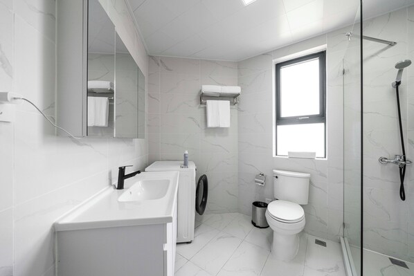 Un baño moderno con lavadora integrada, inodoro y cabina de ducha con paredes de vidrio.