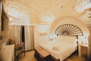 Ein Schlafzimmer mit Steindecke, einem Bett mit weißer Bettwäsche, einer Bank, einem Sessel und einem Nachttisch mit Lampe.