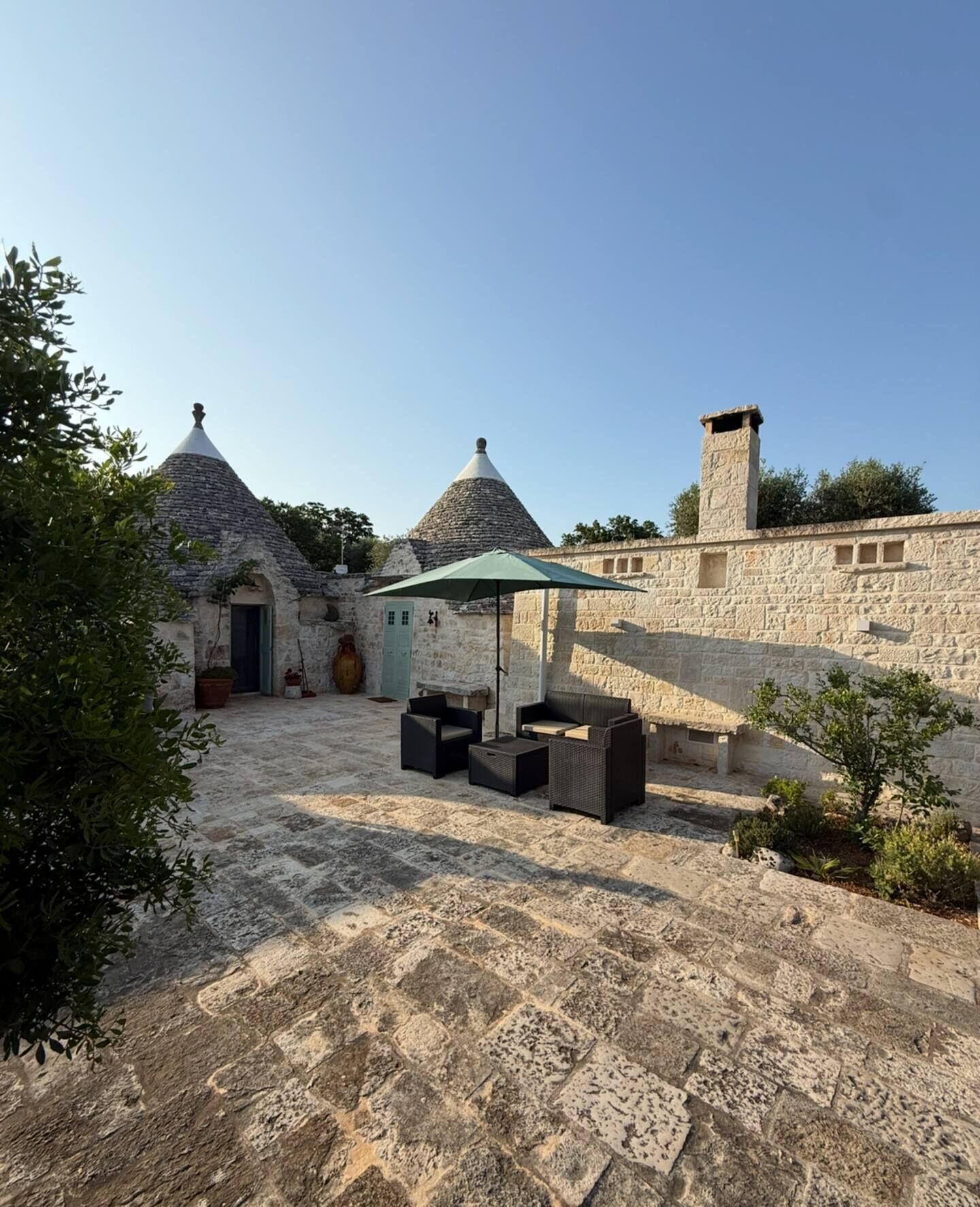A courtyard with stone buildings, outdoor furniture, and a stone wall.