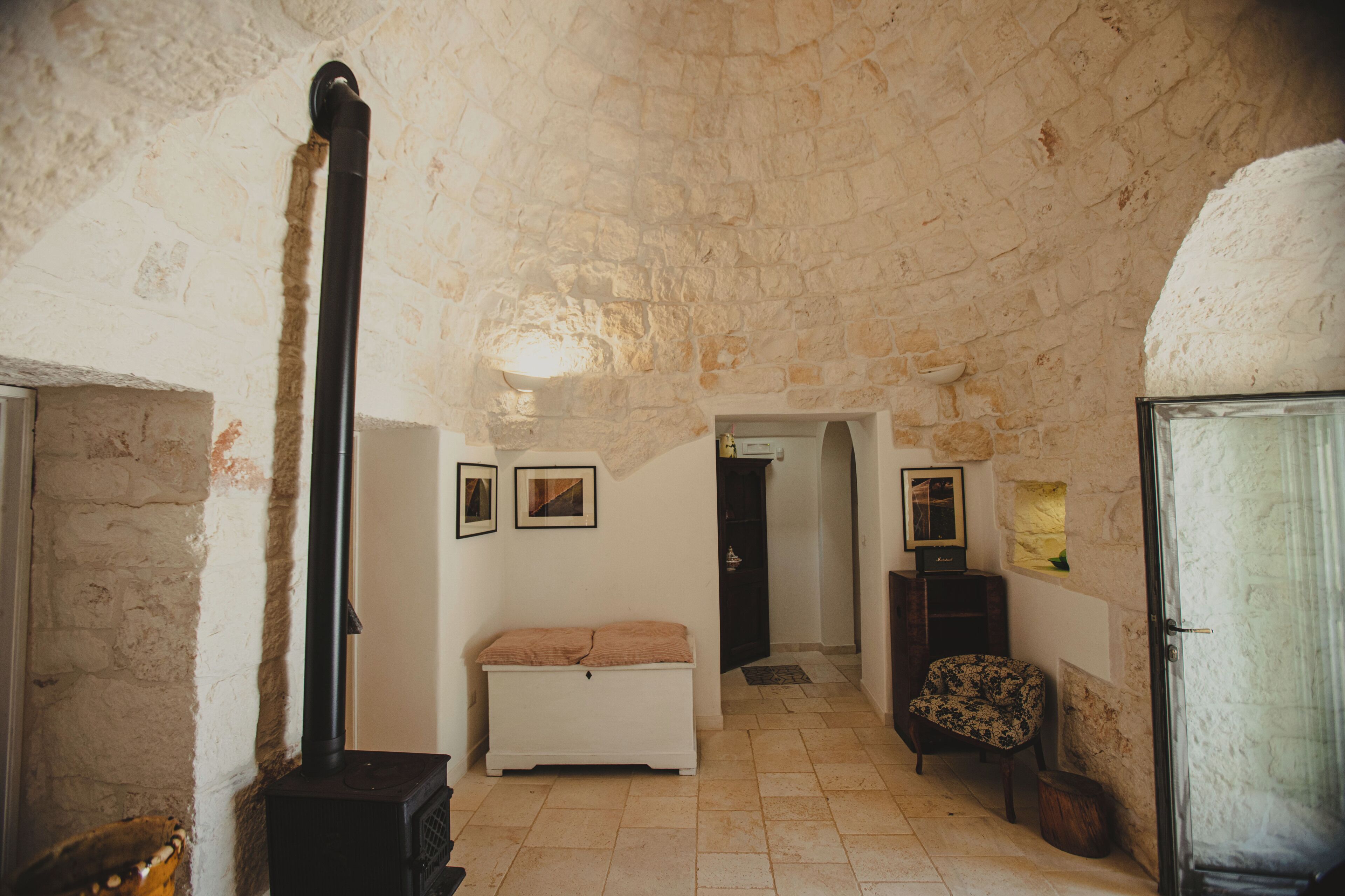 Una habitación de paredes de piedra con chimenea, un banco, una silla y cuadros enmarcados.