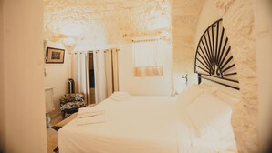 Une chambre avec un plafond en pierre, un lit recouvert de draps blancs, une chaise et un tableau accroché au mur.