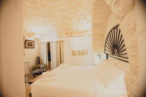 A bedroom with a stone ceiling, a bed with white linens, a chair, and a picture on the wall. - Esclusivo Trullo con piscina (Cisternino)