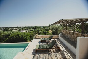 A rooftop pool with lounge chairs, a stone wall, and a view of the city.