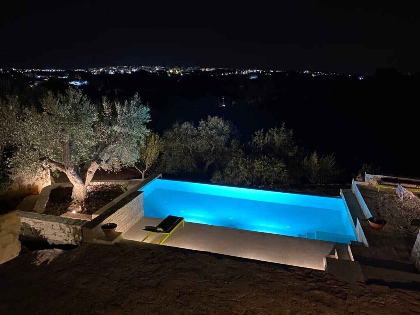 A rectangular swimming pool with a view of a cityscape at night.