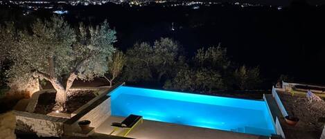 A rectangular swimming pool with a view of a cityscape at night.