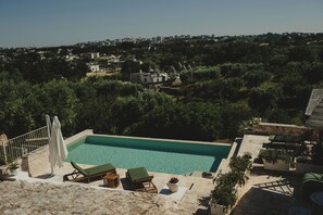 A swimming pool with lounge chairs, a stone deck, and a view of a residential area. - Esclusivo Trullo con piscina (Cisternino)