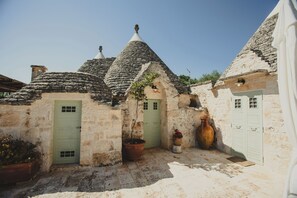 Ein Steinhaus mit einer grünen Tür, einem großen Topfpflanzen und einem mit Fliesen belegten Innenhof.