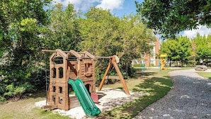 Une aire de jeux avec une structure d’escalade en bois et un toboggan vert.