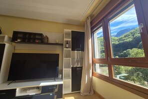 A room with a large window, a flat-screen TV, built-in shelves, and a wooden cabinet.