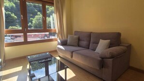 A living room with a sofa, a glass coffee table, and a large window with curtains. - 21A07 Apartment in Felechosa by R2R Consulting (Aller)