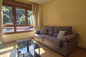 A living room with a sofa, a glass coffee table, and a large window with curtains.