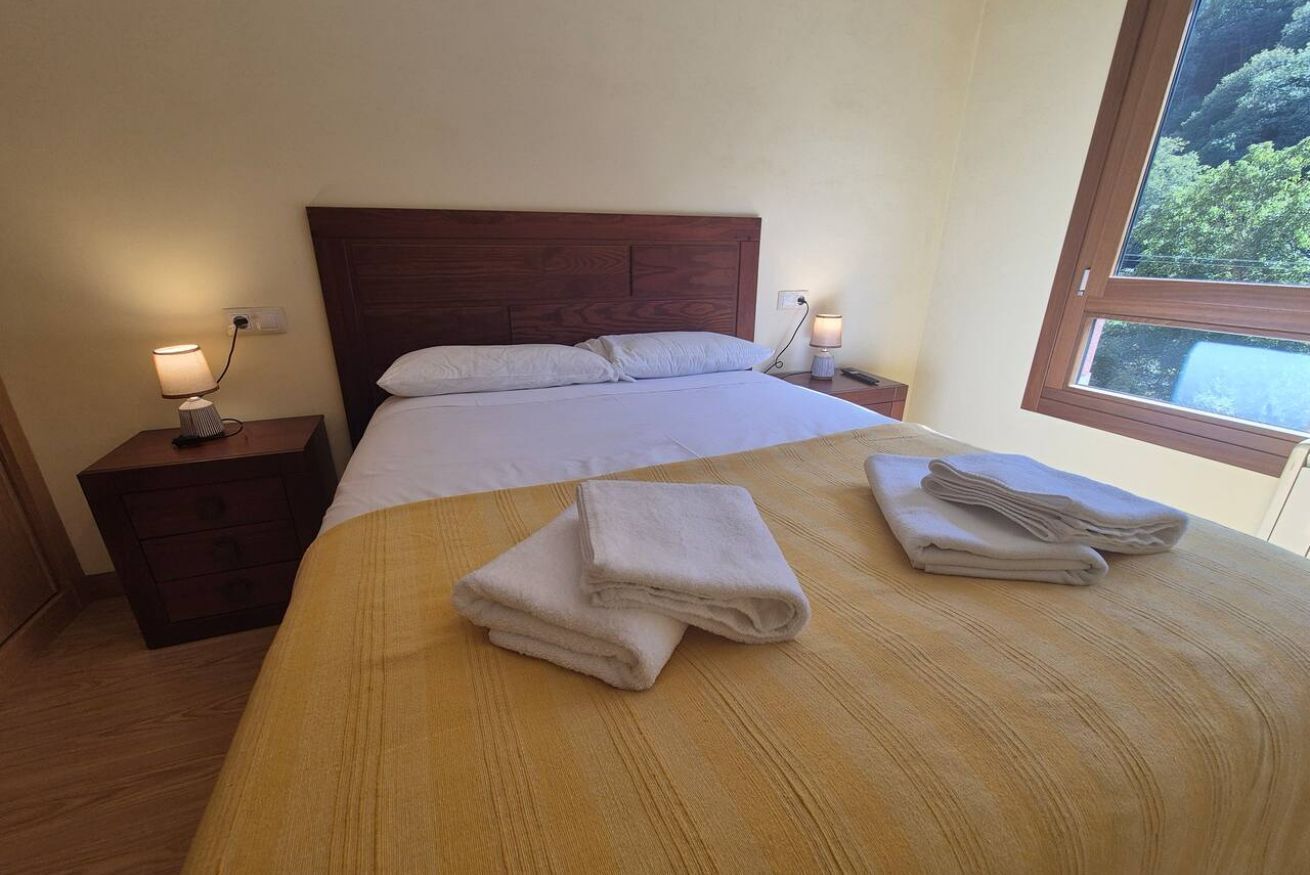 A hotel room with a wooden bed, two bedside tables, a window with a view, and a neatly made bed with folded towels.