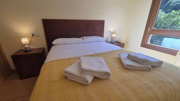 A hotel room with a wooden bed, two bedside tables, a window with a view, and a neatly made bed with folded towels.