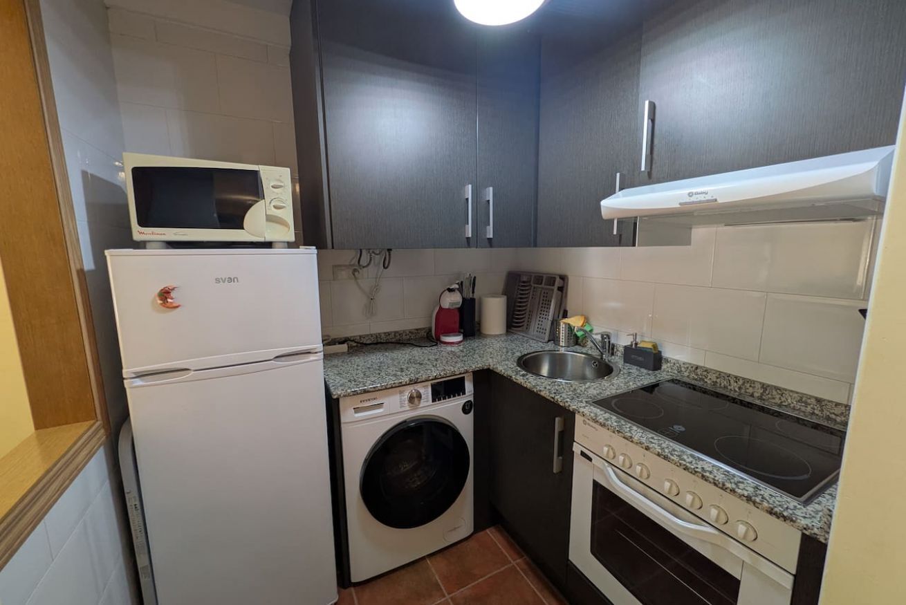 A compact kitchen with a microwave, refrigerator, washing machine, sink, and stove.