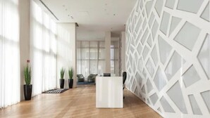 A spacious lobby with a reception desk, potted plants, and a modern geometric wall design. - Luxury Apt Tower Best Sea View Bat Yam (Bat Yam)