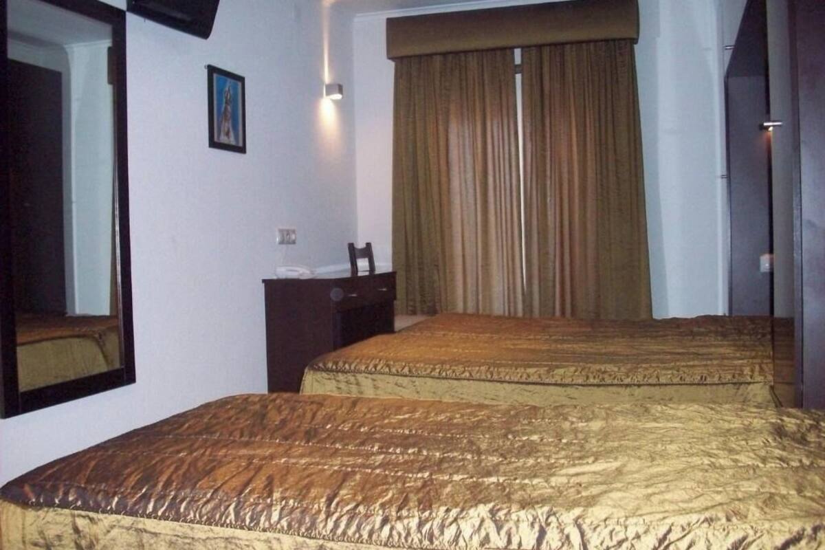 A hotel room with two beds, a large mirror, a nightstand, and a window with curtains.