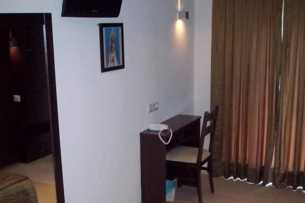 A hotel room with a bed, a desk, a chair, a television mounted on the wall, and a window with curtains.