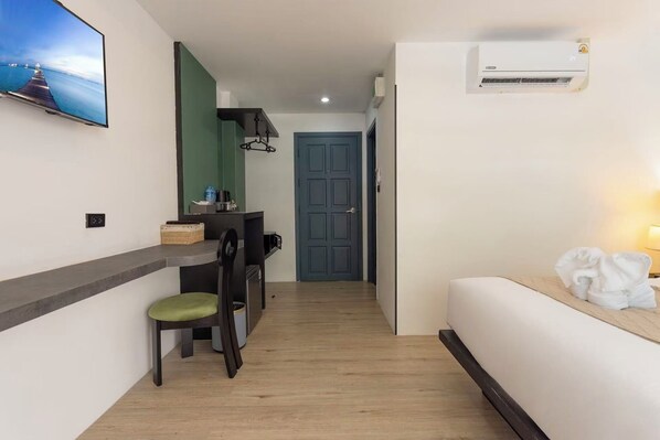 A compact hotel room with a bed, a desk with a chair, a TV mounted on the wall, and an air conditioning unit. - XL Patong Hotel (Patong)