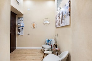 A hallway with a wooden floor, a seating area with a chair and a small table, and a wall-mounted bulletin board with various notices. - Merliani House Holiday Home (Napoli)