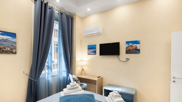 A hotel room with a bed, a desk, a TV, and a window with curtains. - Merliani House Holiday Home (Napoli)