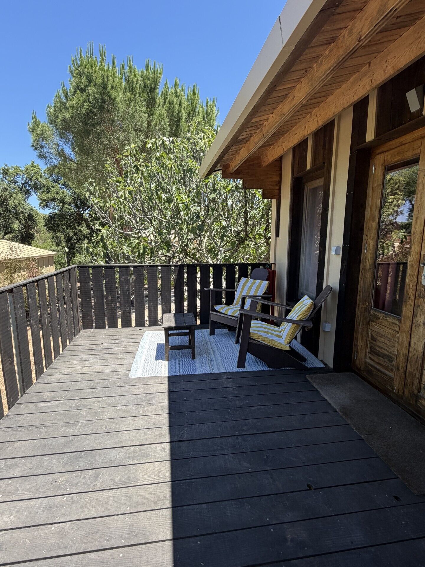A wooden deck with two lounge chairs and a small table, a wooden fence, and a building with a wooden facade.