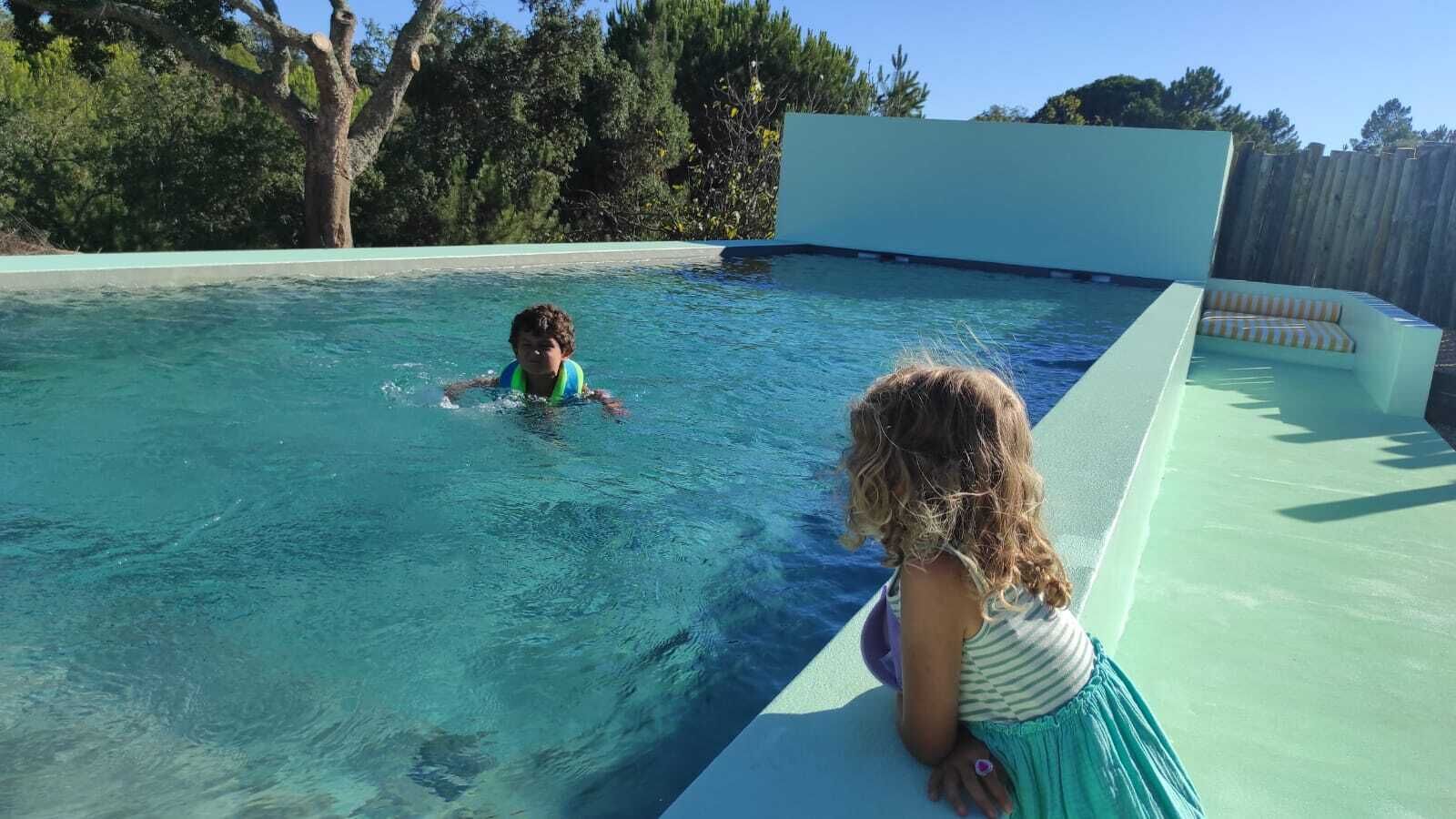 Una piscina con agua cristalina, un niño nadando y otro sentado en el borde.
