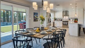 A modern kitchen with a central island, large windows, and a dining area with black chairs. - Pool, Hot Tub + Game Room Near Camelback & Old Town + Trails | Camelback Casa (Phoenix)