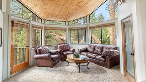 Ein geräumiges Zimmer mit Holzbalkendecke, großen Fenstern, Ledersofas und einem zentral platzierten Couchtisch.