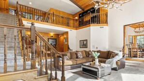 Ein großzügiger Wohnbereich mit einer Holztreppe, einem großen Sofa und einem Essbereich mit hohen Decken und Holzbalken.