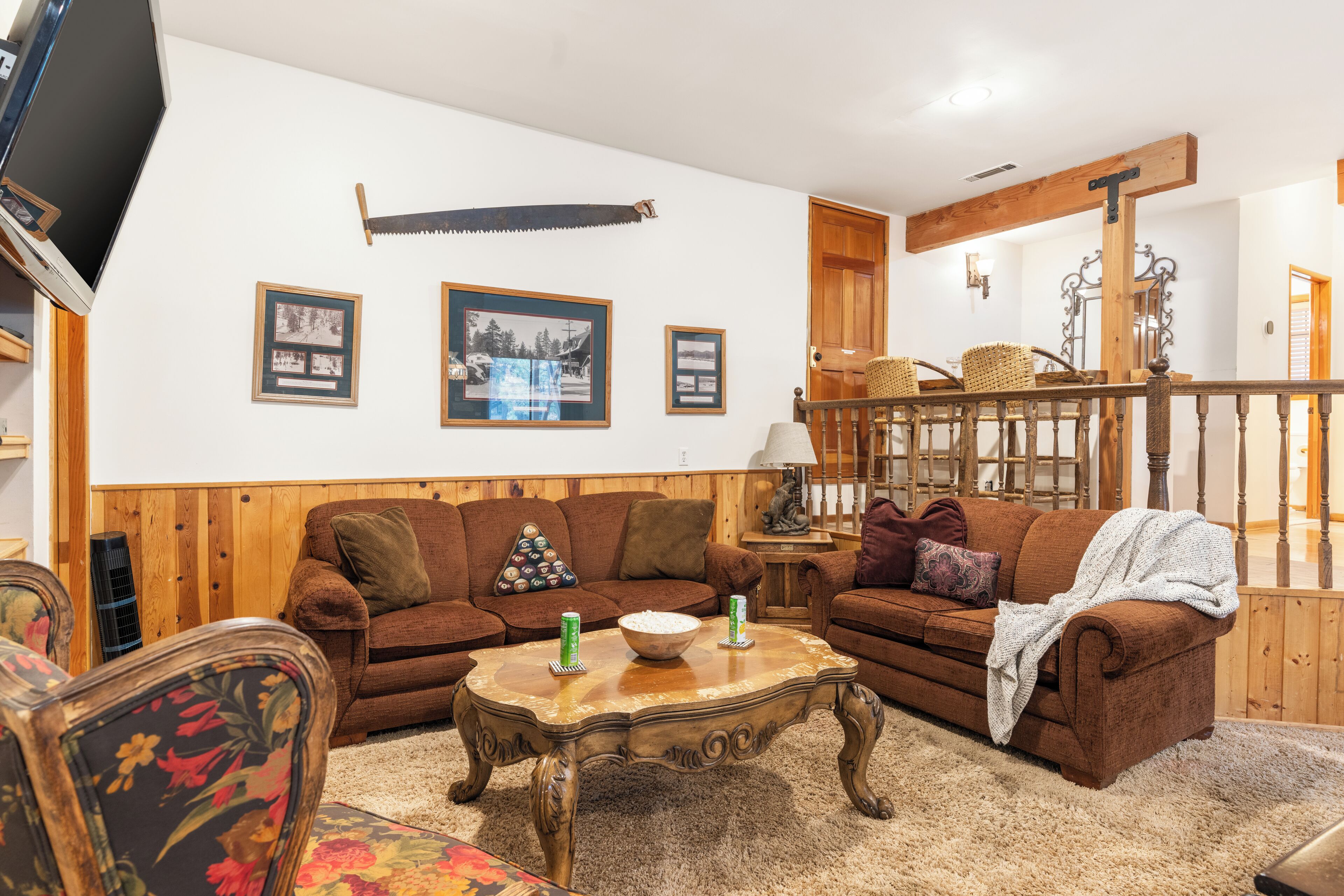 A cozy living room with a wooden floor, a brown sofa, a coffee table, and framed pictures on the wall.