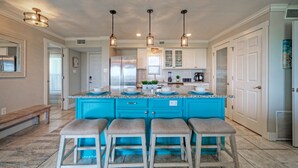 A kitchen with a blue island, four bar stools, stainless steel appliances, and pendant lighting. - Awesome Beachfront | Gulf Views + Pools + Tennis + Pickleball & Beach Access (Port Aransas)