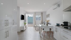 A modern kitchen with white cabinetry, a dining area with a white table and chairs, and a view to the outside.