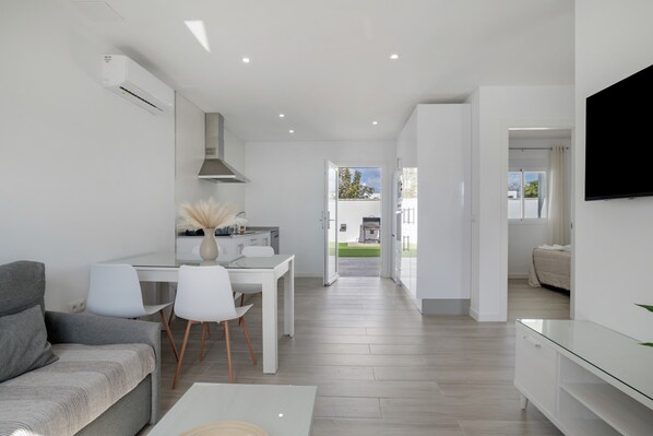 Un salon moderne comprenant un canapé, une table à manger, des chaises et un téléviseur fixé au mur.