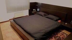 Ein Schlafzimmer mit einem großen Bett, einem Nachttisch, einer Lampe und einem Fenster mit Jalousien.