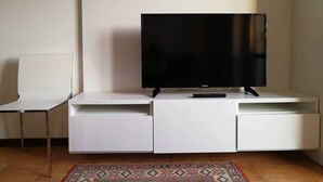 Ein modernes Wohnzimmer mit einem Flachbildfernseher auf einer weißen Unterhaltungseinheit, einem kleinen weißen Sessel und einem gemusterten Teppich.