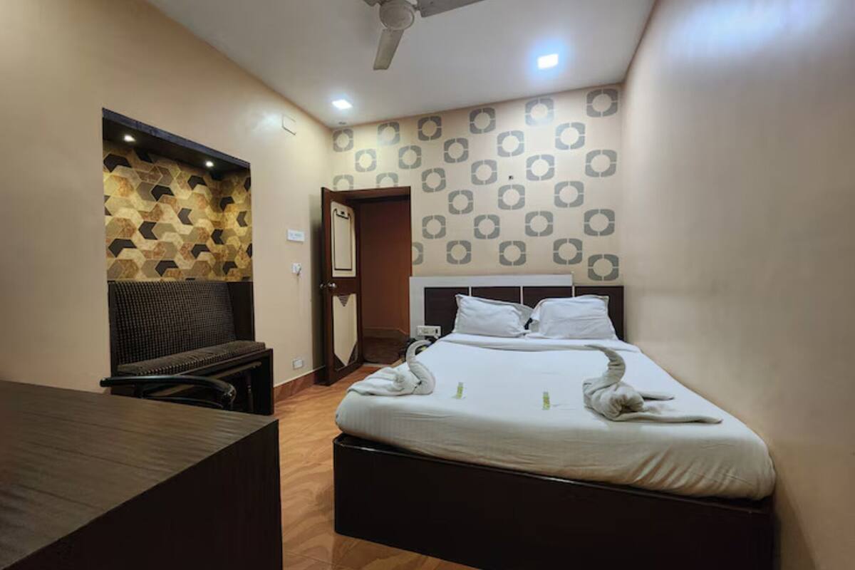 Ein Hotelzimmer mit Bett, Schreibtisch, Stuhl, Deckenventilator und Wandverkleidung mit Muster.