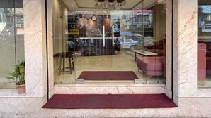 L’entrée d’un hôtel, avec une porte en verre, un tapis rouge et un espace salon à l’intérieur.