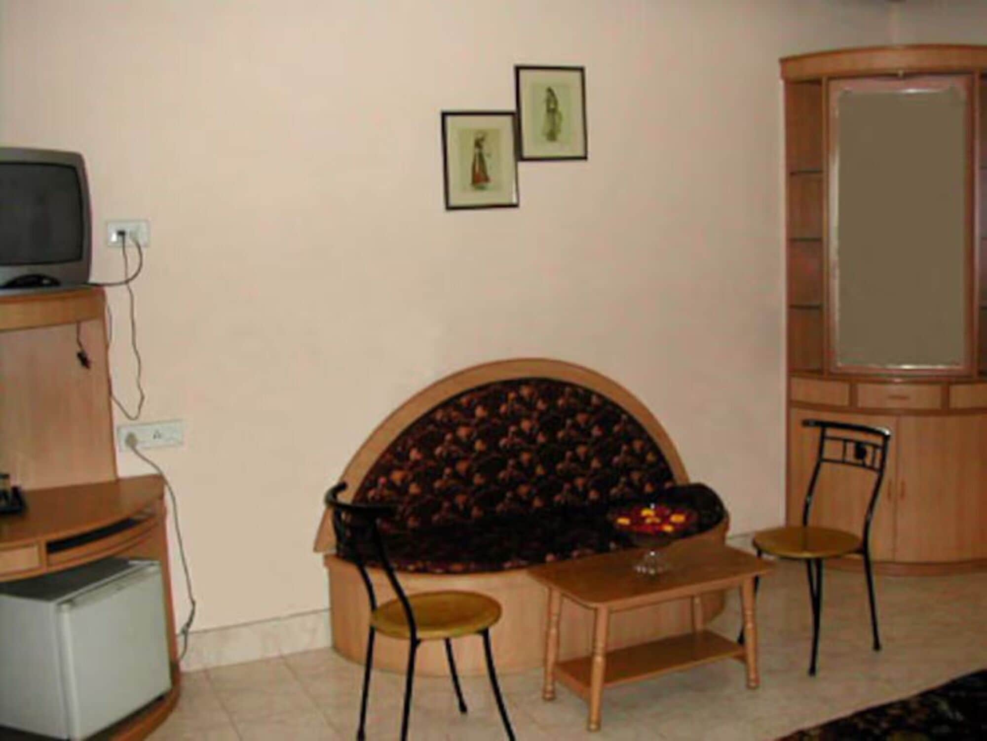 A living room with a sofa, two chairs, a small table, a television, and framed pictures on the wall.