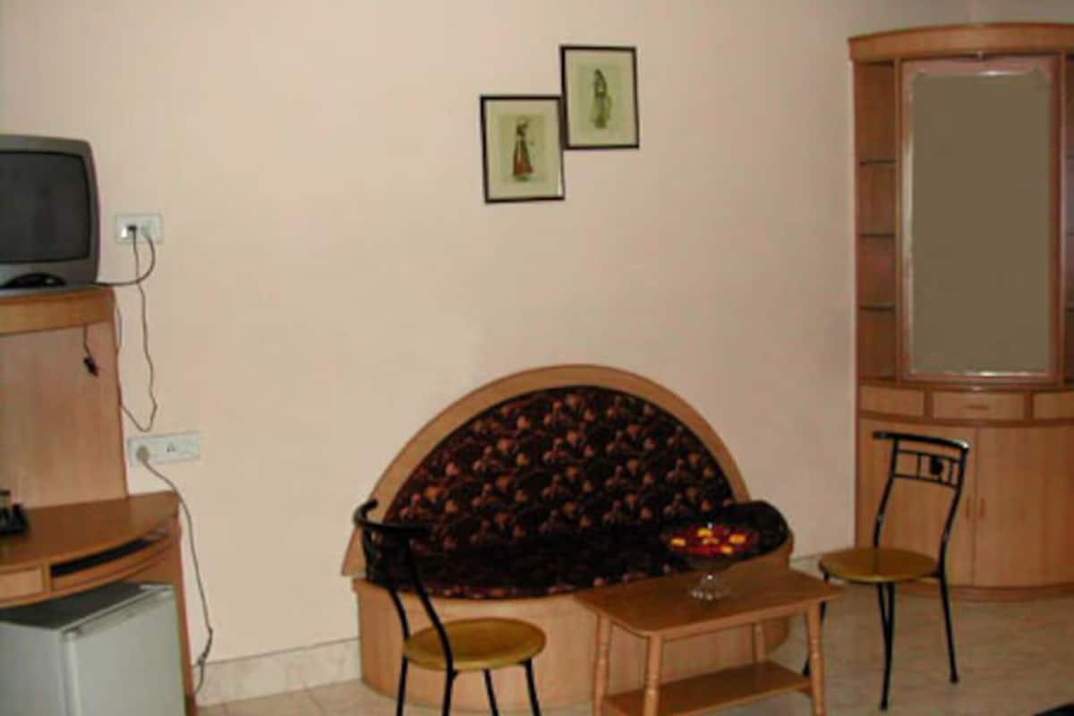 A living room with a sofa, two chairs, a small table, a television, and framed pictures on the wall.