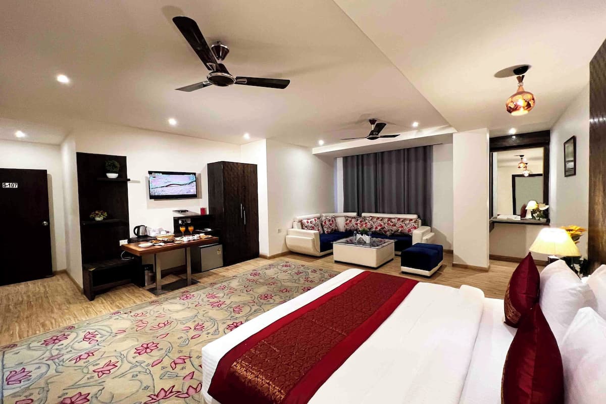 A hotel room with a bed, a sofa, a desk with a computer, a television, and a ceiling fan.
