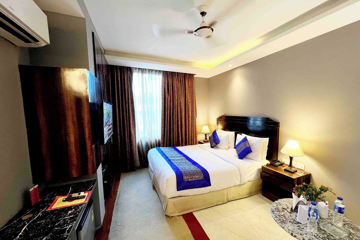 A hotel room with a bed, a TV, a desk, a lamp, and a ceiling fan.