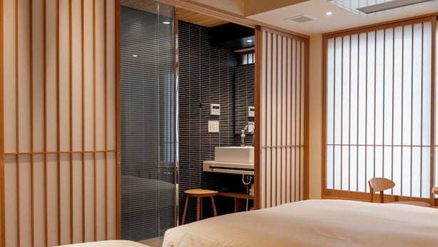 Un dormitorio moderno con dos camas, un escritorio con silla y una puerta corredera que da a un baño.