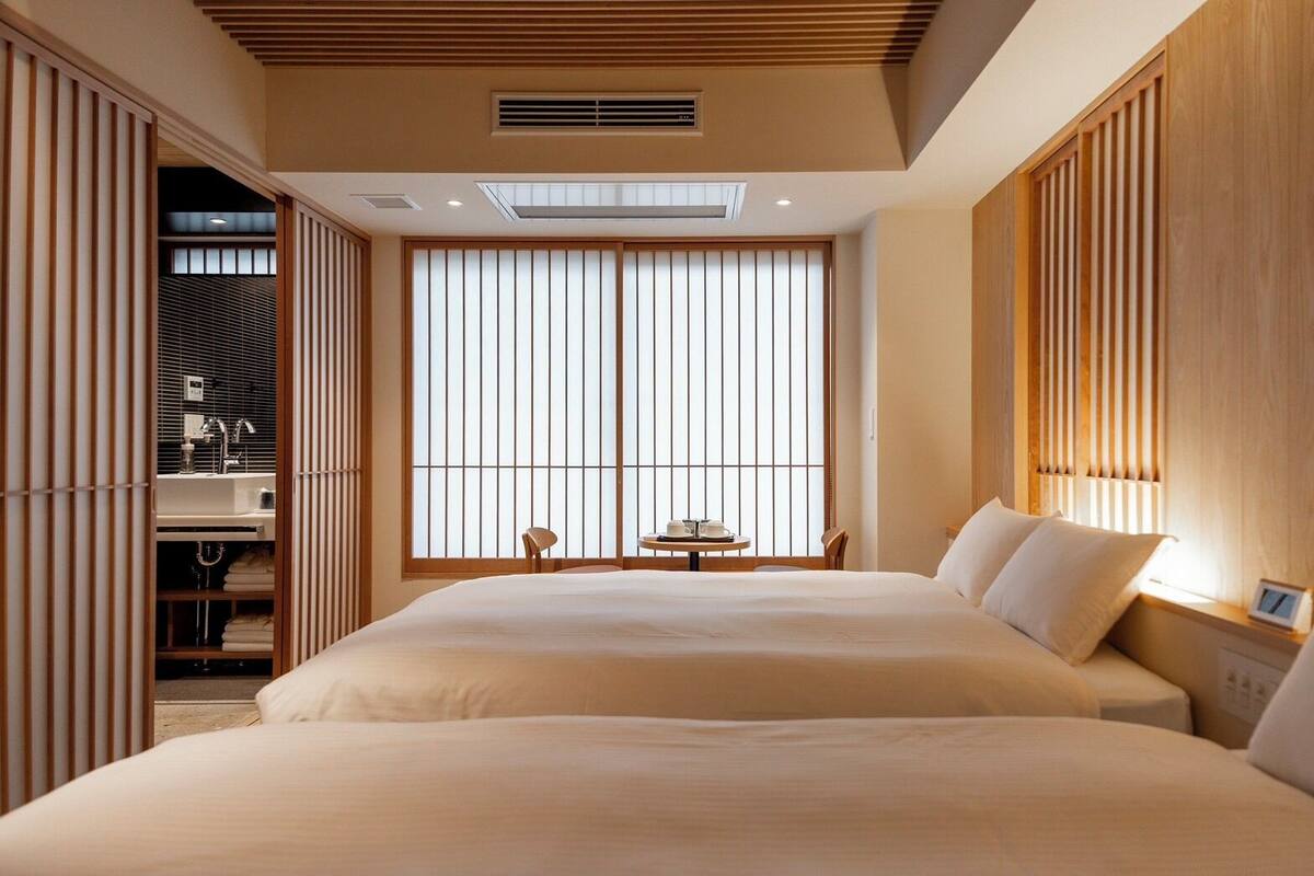 Een hotelkamer met twee bedden, een tafeltje en uitzicht door een shoji-scherm.