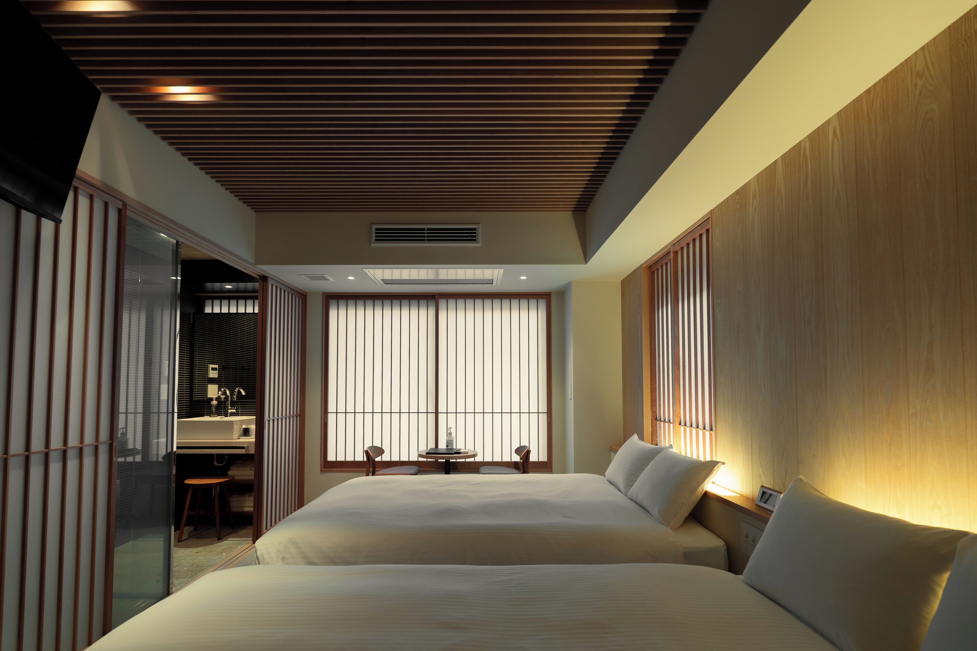 Ein Hotelzimmer mit zwei Betten, einer Sitzecke mit Tisch und Stühlen, einem großen Fenster mit Vorhängen und einer Holzbalkendecke.