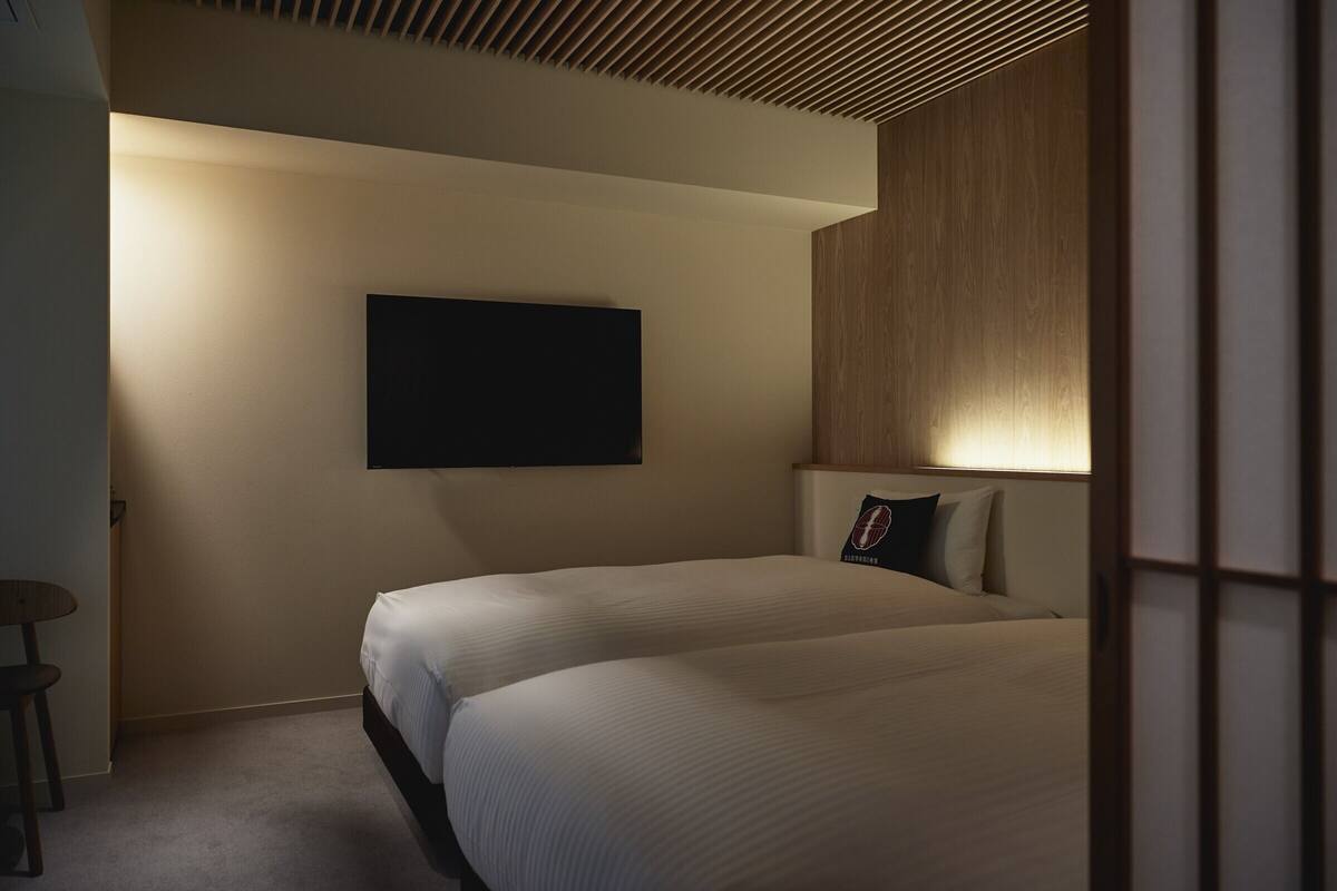 Een hotelkamer met twee bedden, een flatscreen televisie aan de wand en een klein tafeltje met een stoel.