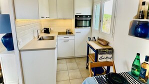 Cocina compacta con armarios blancos, horno empotrado y comedor con una mesa lista para dos.